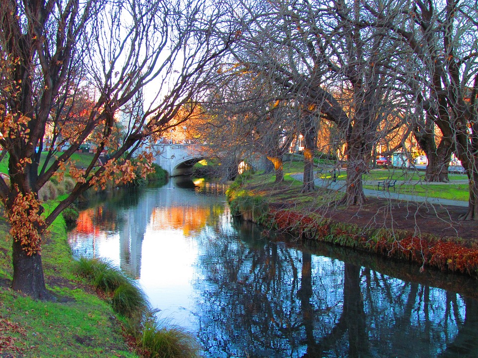 Ruhiger Fluss mit Bäumen an den Ufen, im Hintergrund eine steinerne Bogenbrücke, herbstliche Stimmung